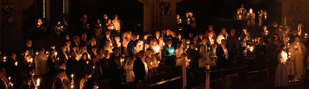 A large group of people are standing in a dark church with candles.