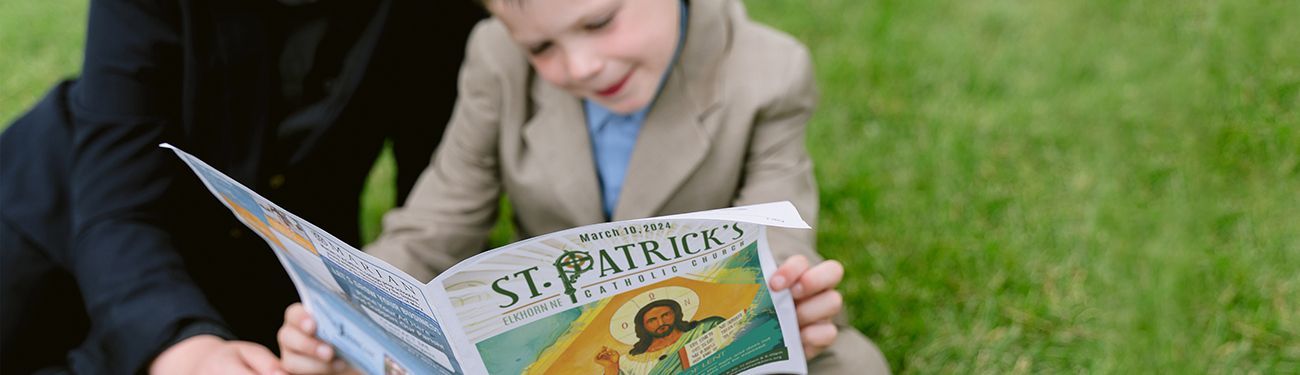 A little boy in a suitcoat  is reading a bulletin.