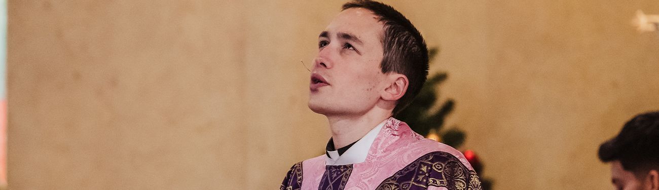A Priest in a pink robe is standing in front of a Christmas tree.