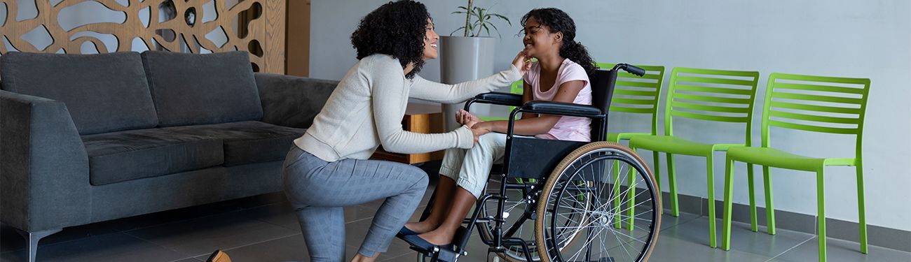 A woman is kneeling down next to a girl in a wheelchair.