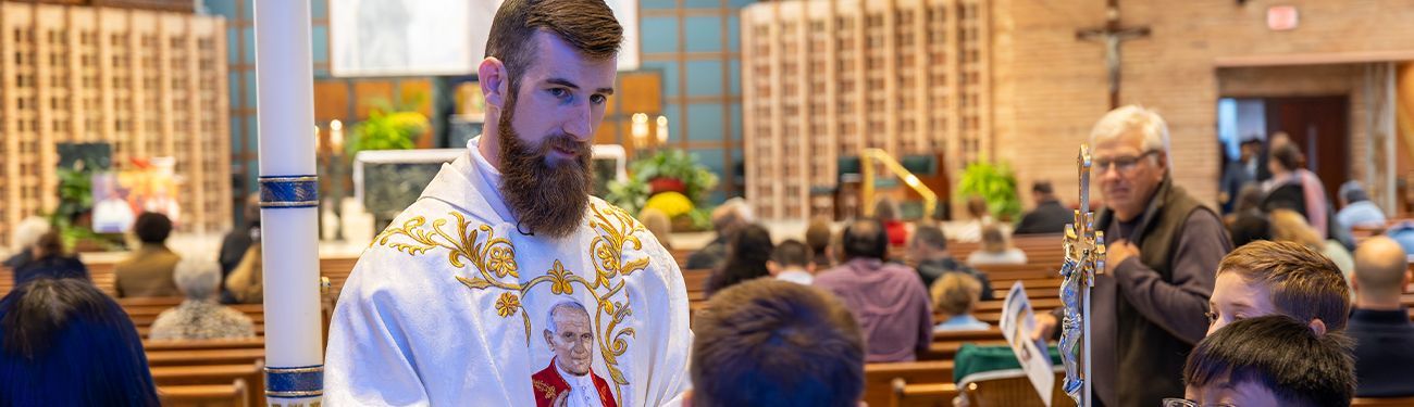 A priest with a beard is holding a candle in a church.