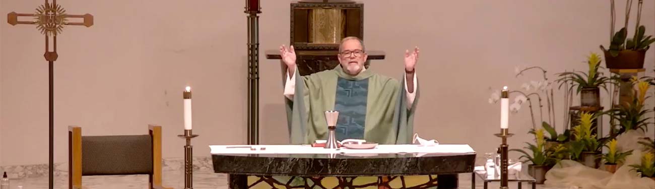 A Priest behind a table with his hands raised.