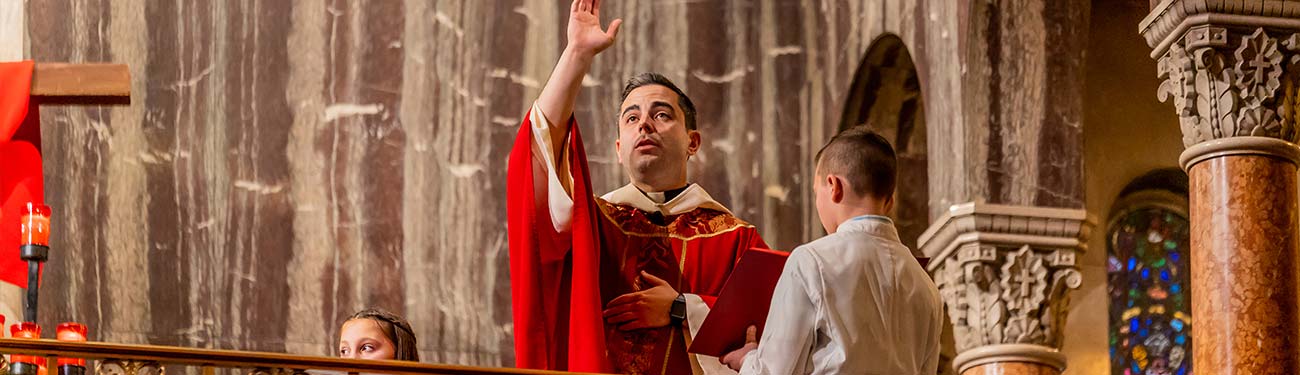 A priest in a red robe is giving a blessing in a church.