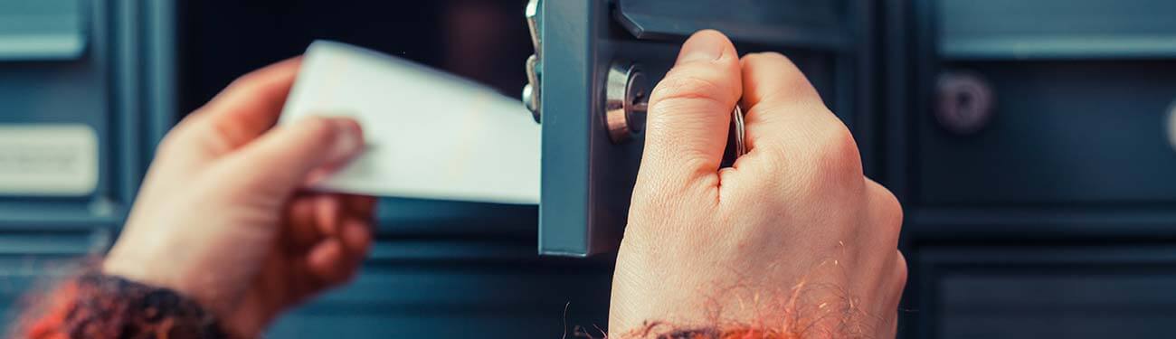 A person is putting an envelope in a mailbox.