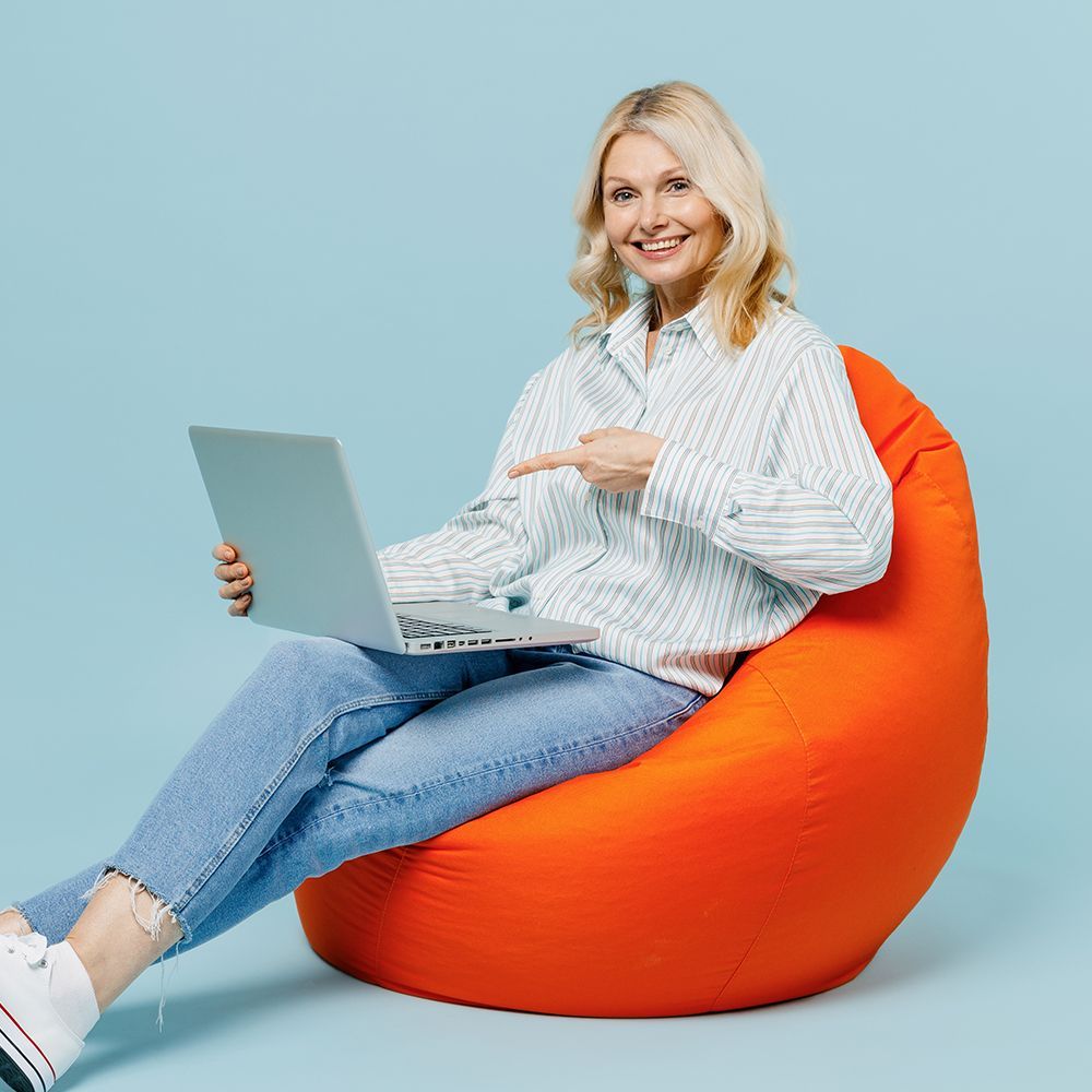 Woman sitting on an orange beanbag using a laptop against a light blue background
