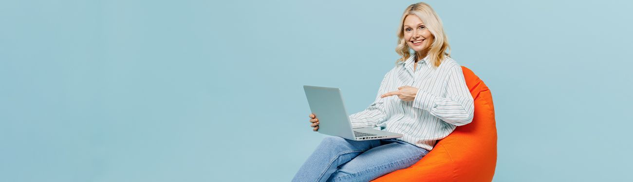 Woman sitting on an orange beanbag using a laptop against a light blue background