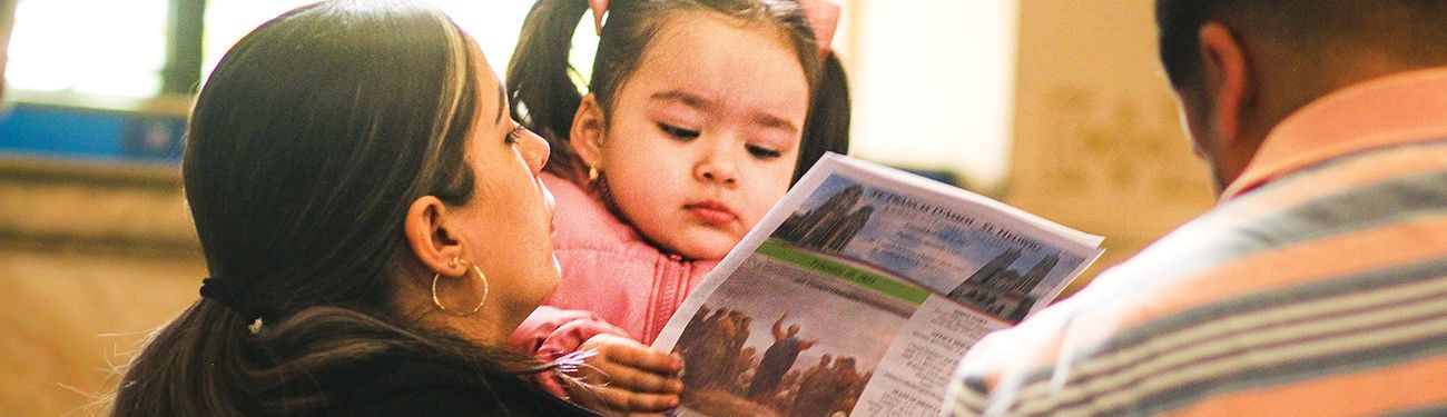 A woman is holding a little girl while she is holding a bulletin.