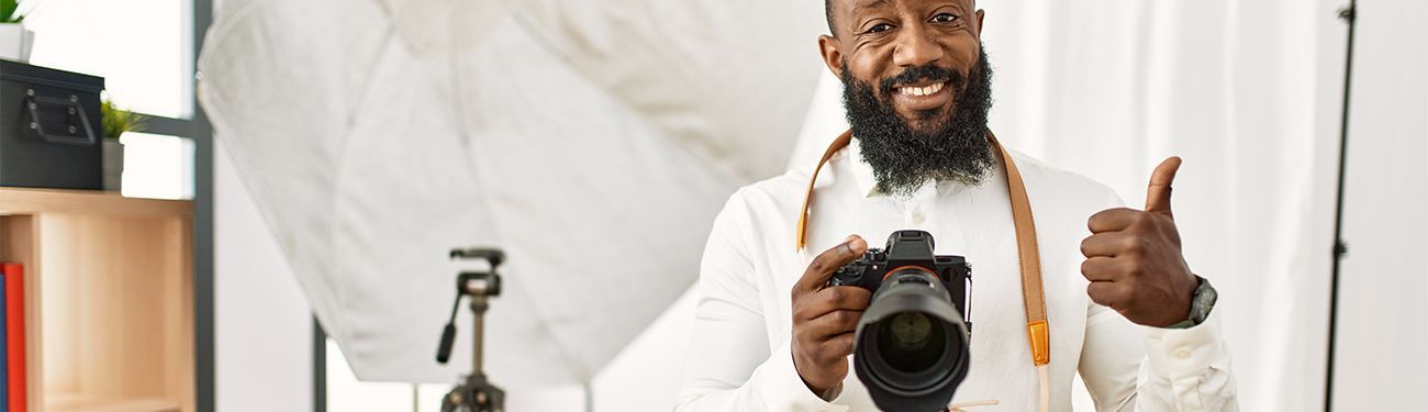 A man with a beard is holding a camera and giving a thumbs up.