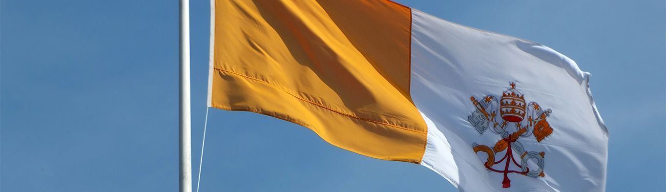 Photo of the Vatican flag flying against a blue sky. 