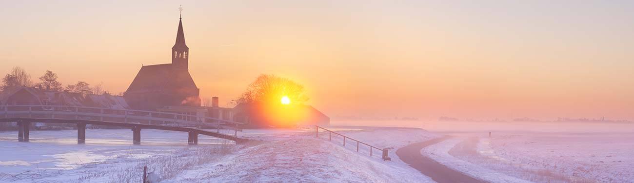 The sun is setting over a snowy field with a church in the background.