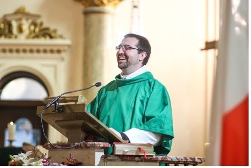A Priest in a green robe is giving a speech at a podium.