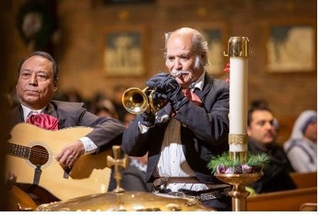 A man is playing a trumpet in a church while another man plays a guitar.