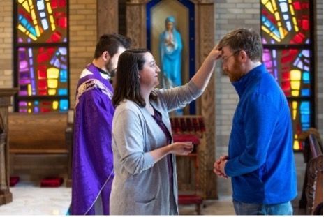 A woman is washing a man 's forehead in a church.
