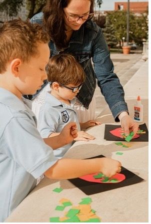 A woman is helping two young boys with their crafts.