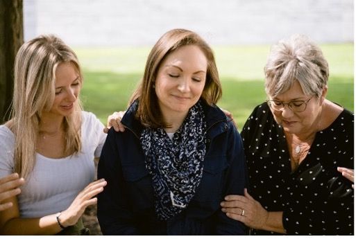 Three women are sitting next to each other under a tree.