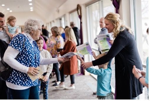 A woman is giving a child a book while standing next to a group of people.