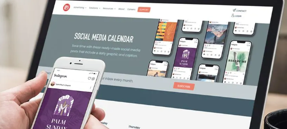 A person is holding a cell phone in front of a laptop showing a social media calendar.