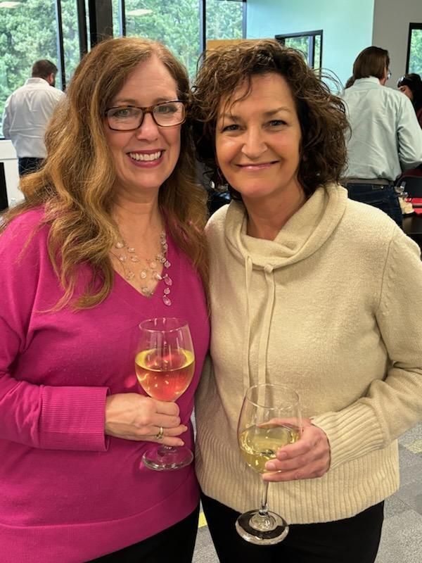 Two women are posing for a picture while holding wine glasses.