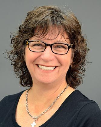 A woman wearing glasses and a necklace is smiling for the camera.