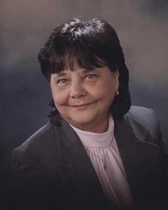 A woman in a suit and pink shirt is smiling for the camera.