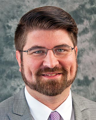 A man with a beard and glasses is wearing a suit and tie.