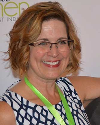 A woman wearing glasses and a green lanyard smiles for the camera.