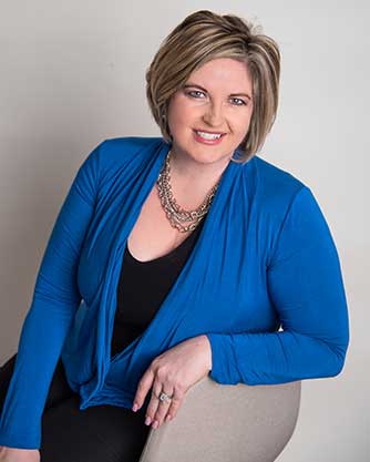 A woman wearing a blue cardigan and a necklace is sitting on a chair.