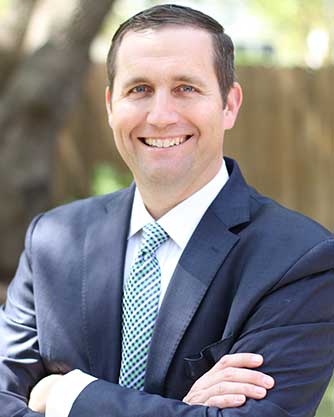 A man in a suit and tie is smiling with his arms crossed.
