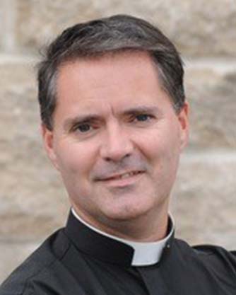 A man wearing a priest's collar is smiling for the camera.