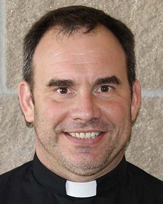 A man wearing a priest's collar is smiling for the camera.