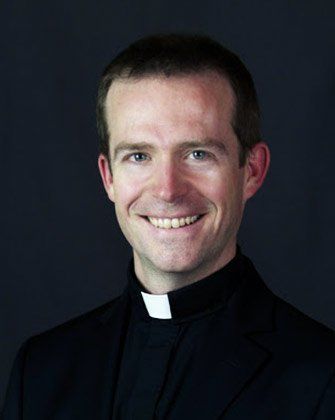 A man in a black suit and white collar is smiling for the camera.