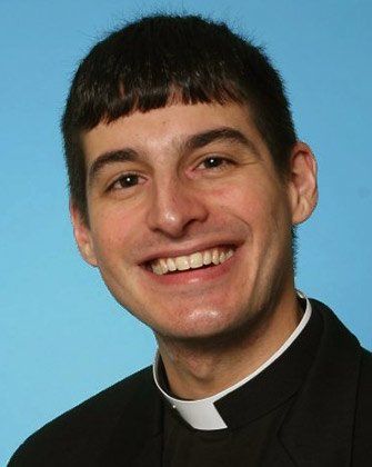 A man in a clergy collar is smiling for the camera.