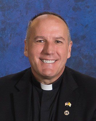 A man in a clergy collar is smiling for the camera.