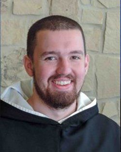 A man with a beard is wearing a black robe and smiling.