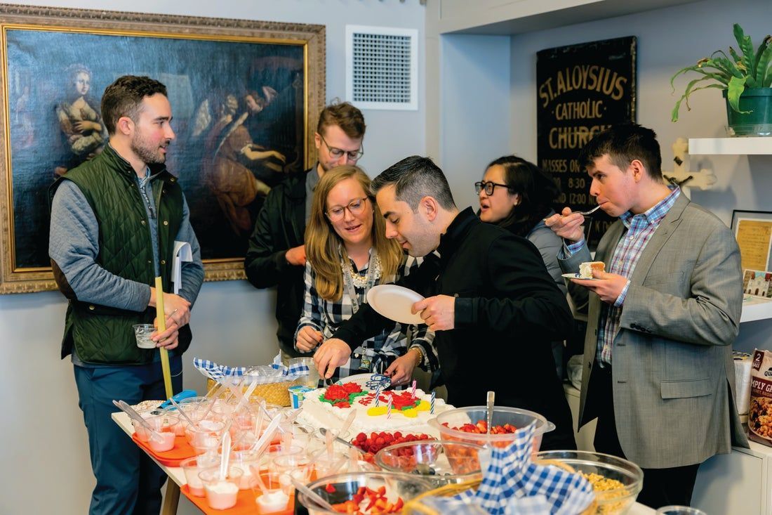 A group of people are standing around a table eating food.