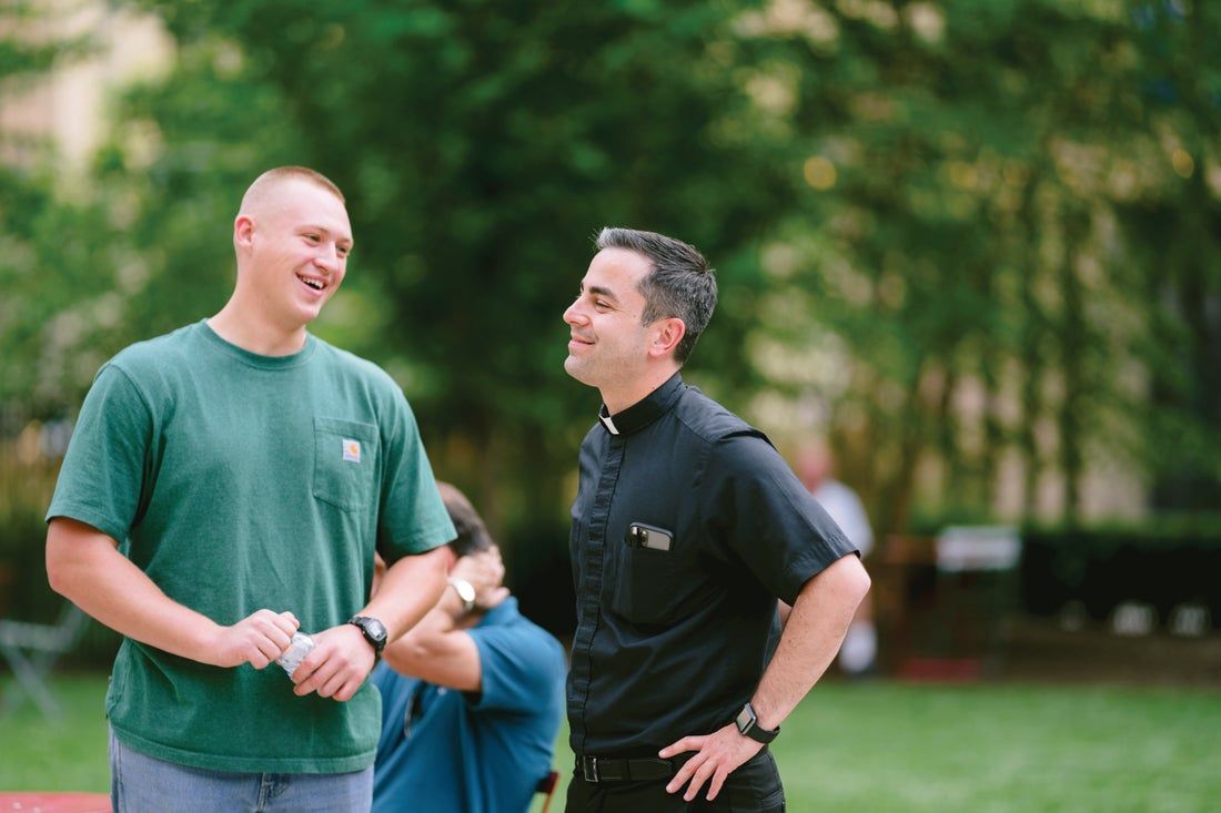 Two men are standing next to each other in a park talking to each other.