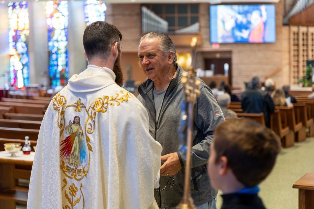 A Priest is talking with a man in the back of a church.