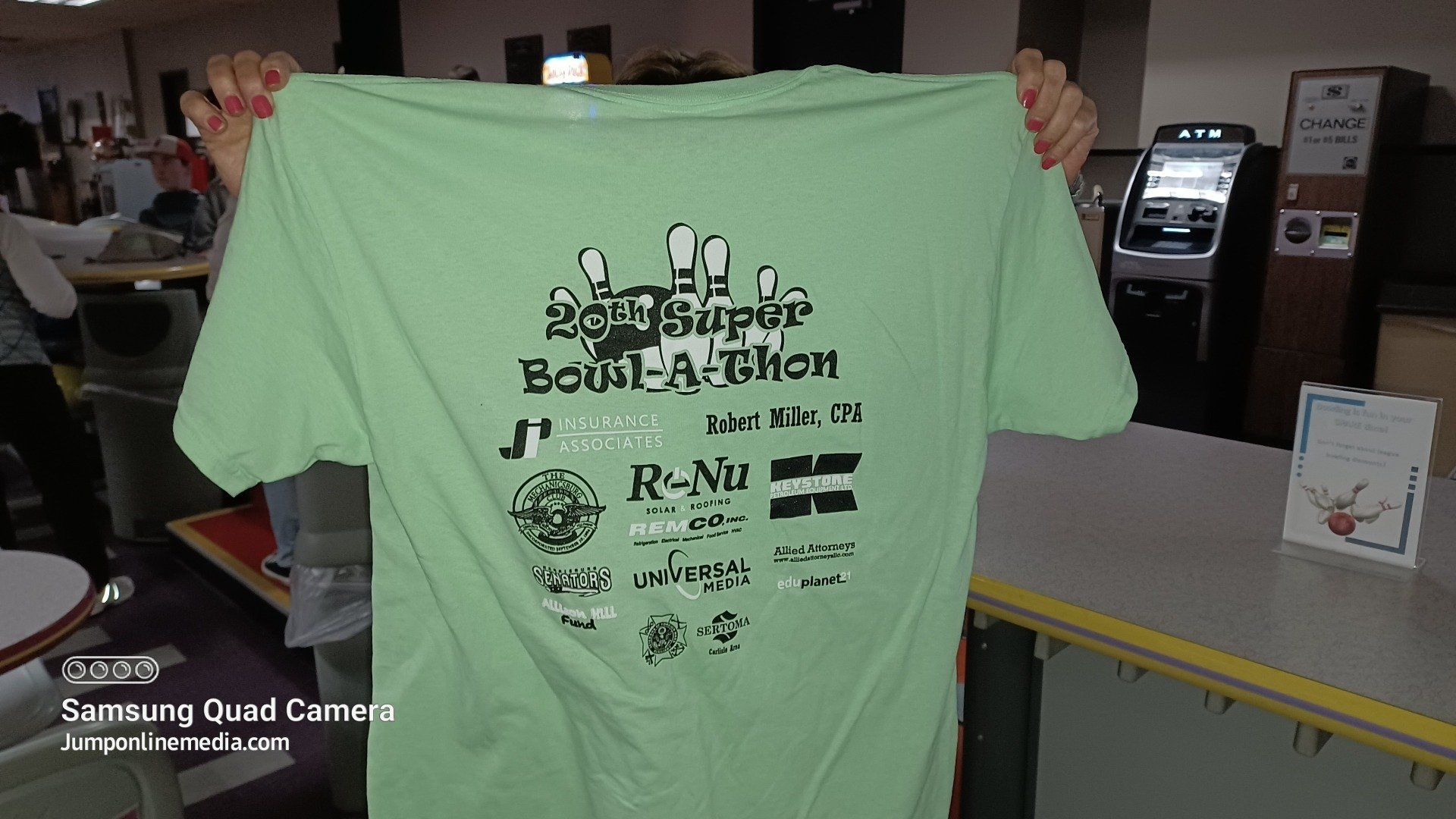 A person is holding up a green t-shirt that says re-nu