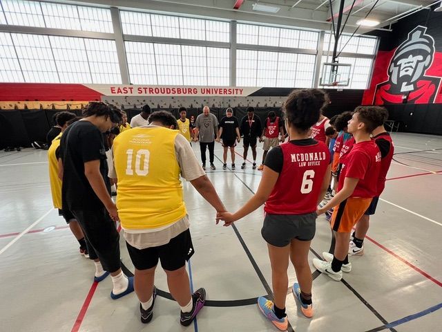 A group of young men are standing in a circle on a basketball court holding hands.
