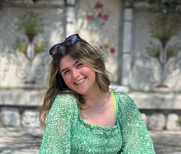 A woman in a green dress and sunglasses is smiling for the camera.
