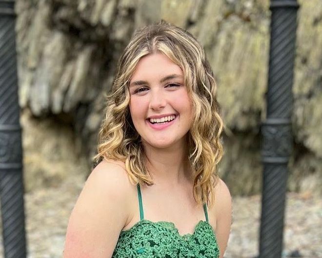 A young woman in a green dress is smiling for the camera.