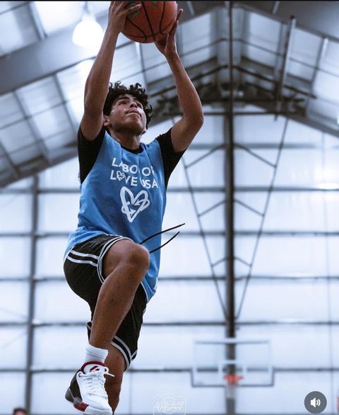 A man in a black tank top with a triangle on it is jumping in the air with a basketball