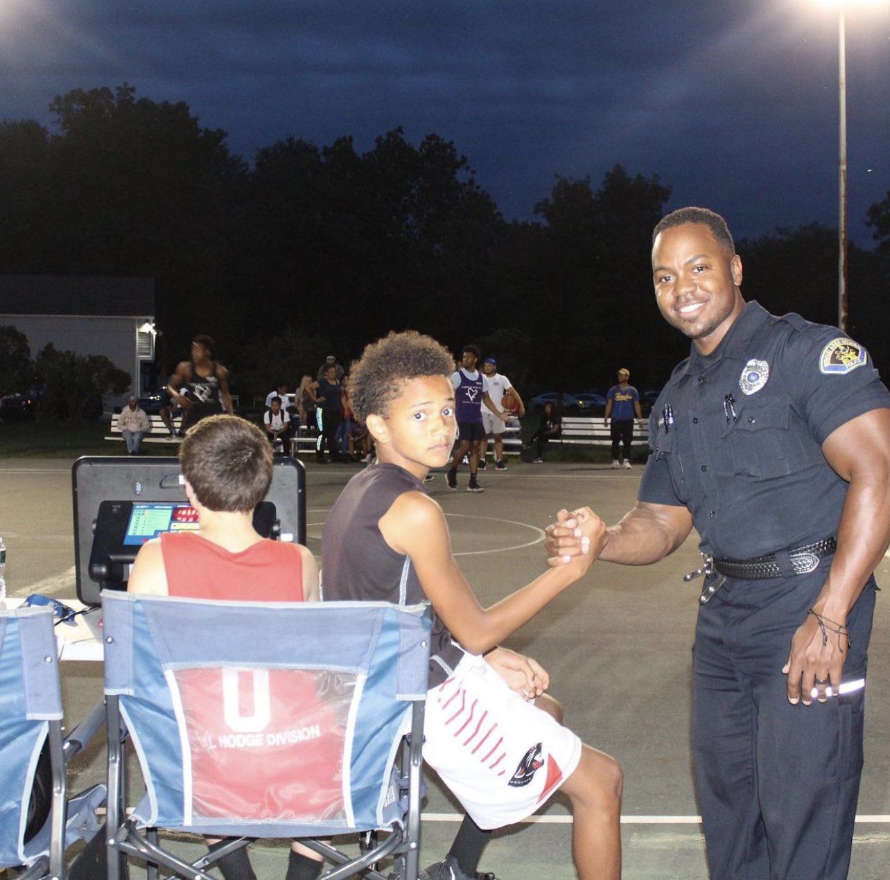 A man in a police uniform shakes hands with a boy in a chair with the letter u on it