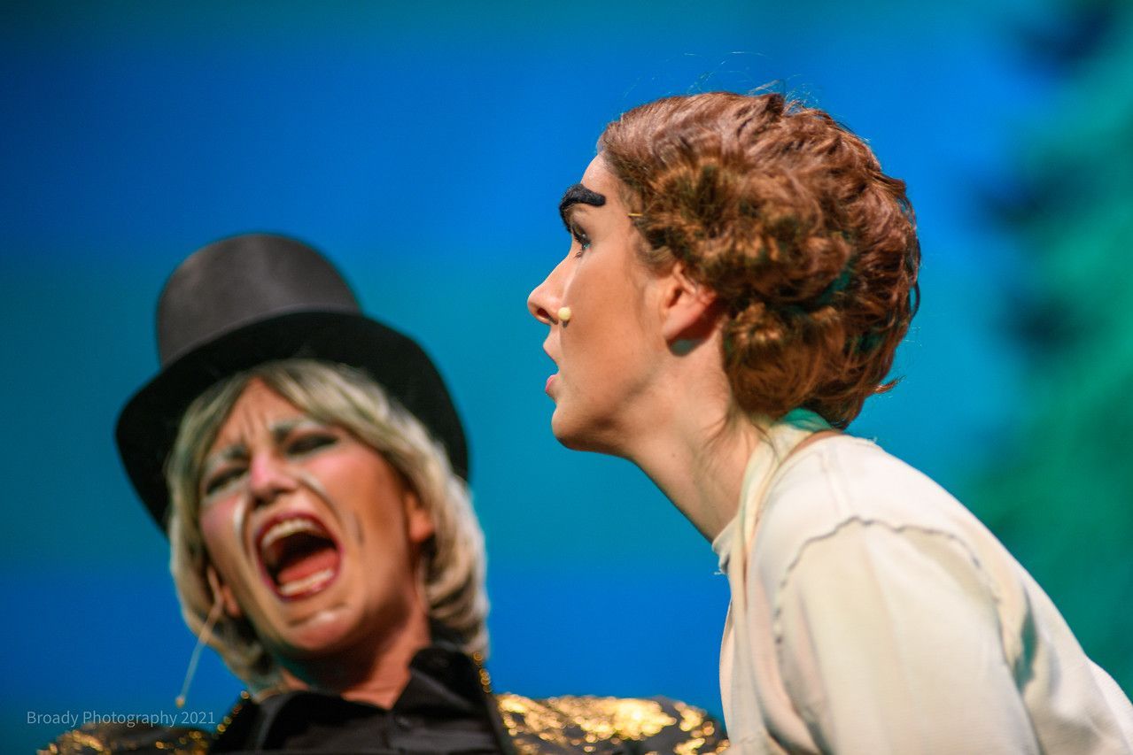 Two women are standing next to each other on a stage and one of them is wearing a top hat.