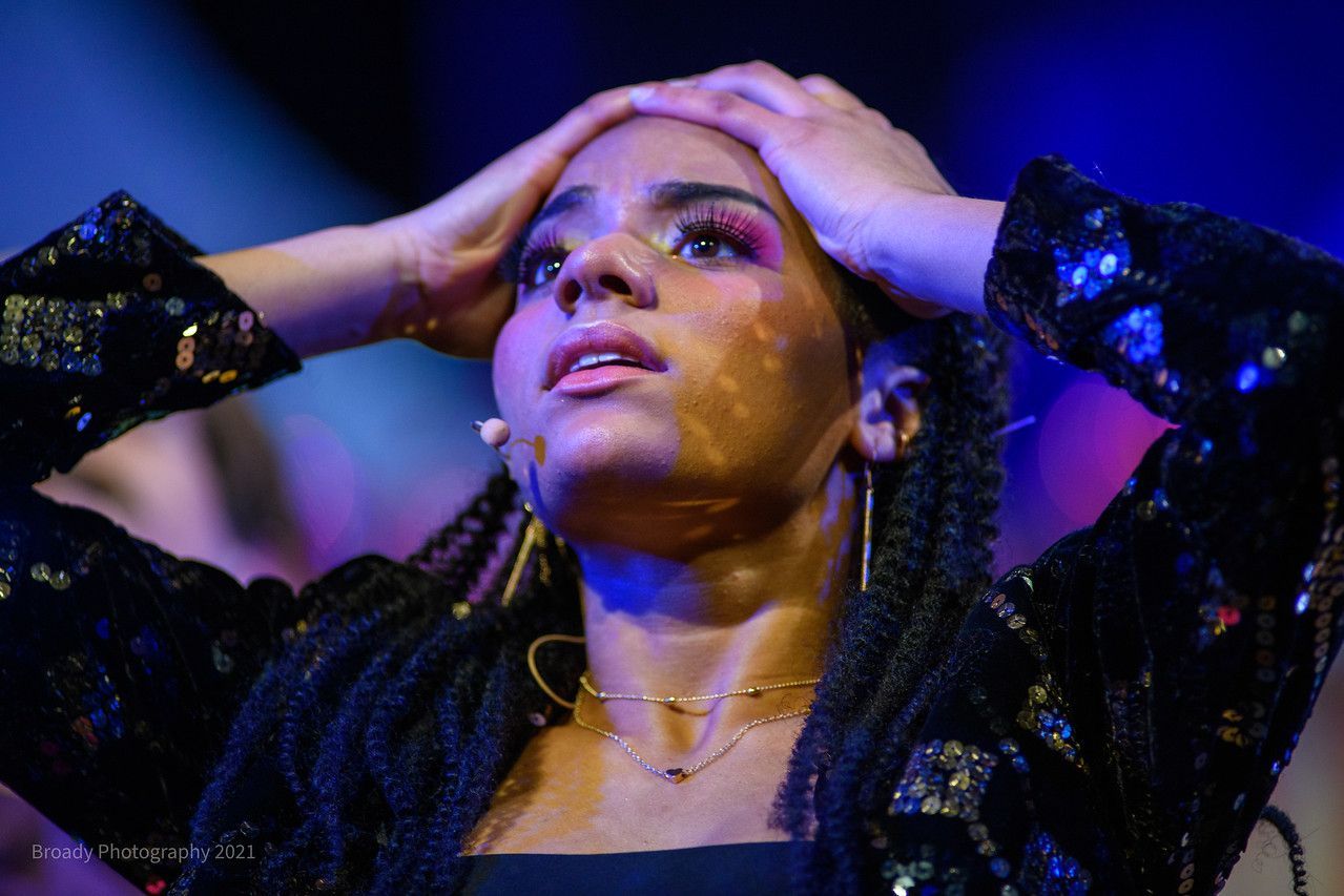 A woman with braids is holding her head in her hands.