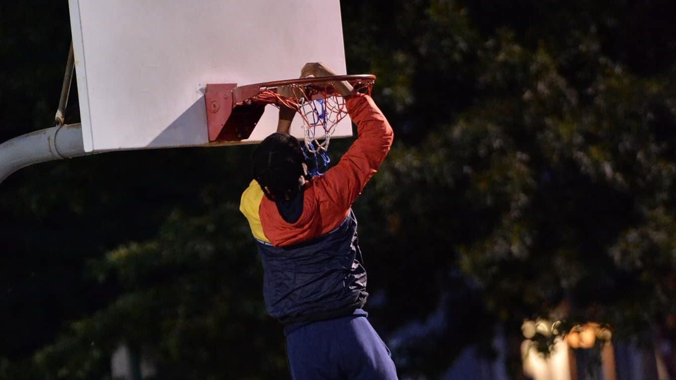 A man is dunking a basketball into a hoop at night.
