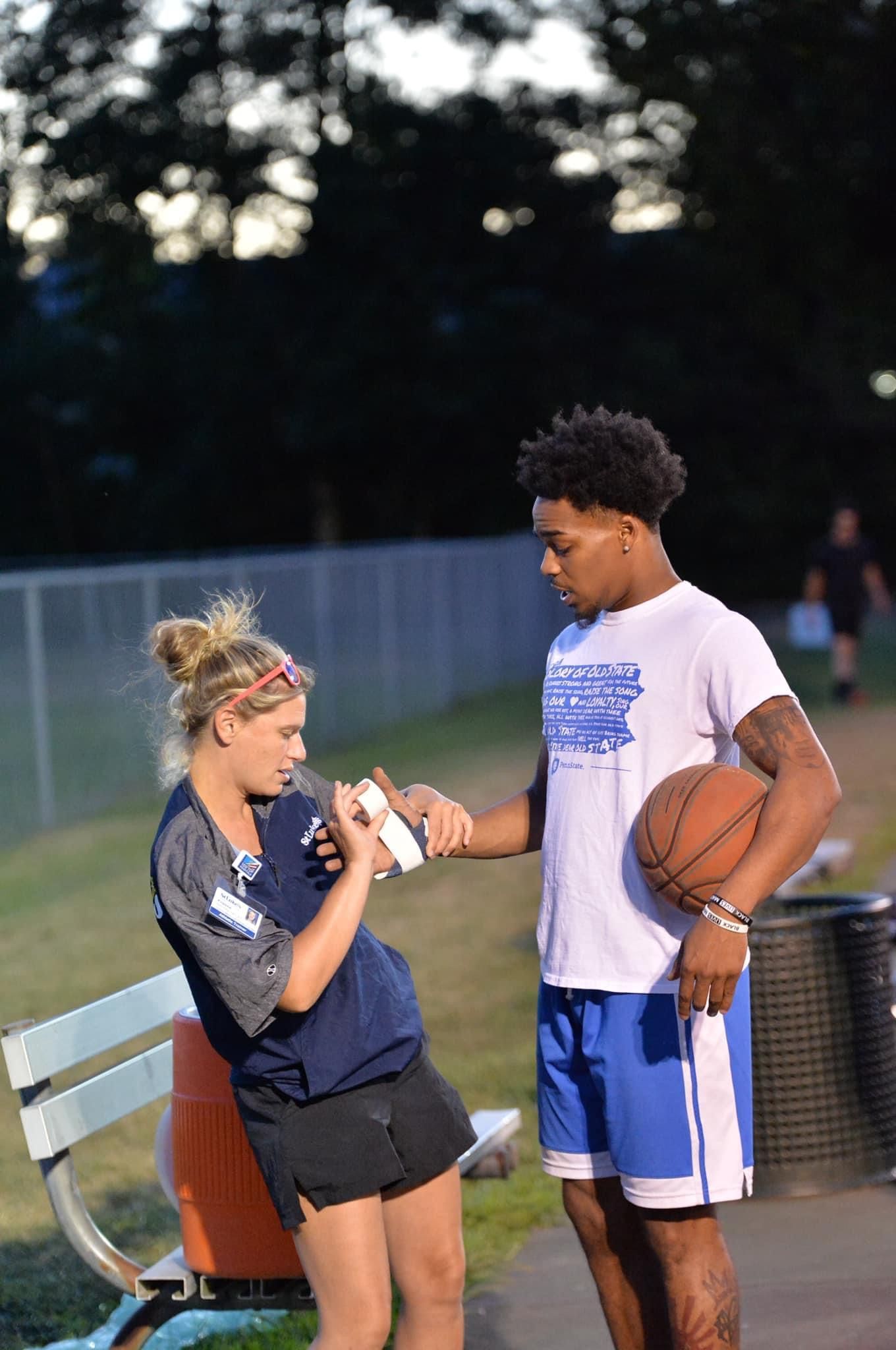 A man and a woman are shaking hands in a park while a man holds a basketball.