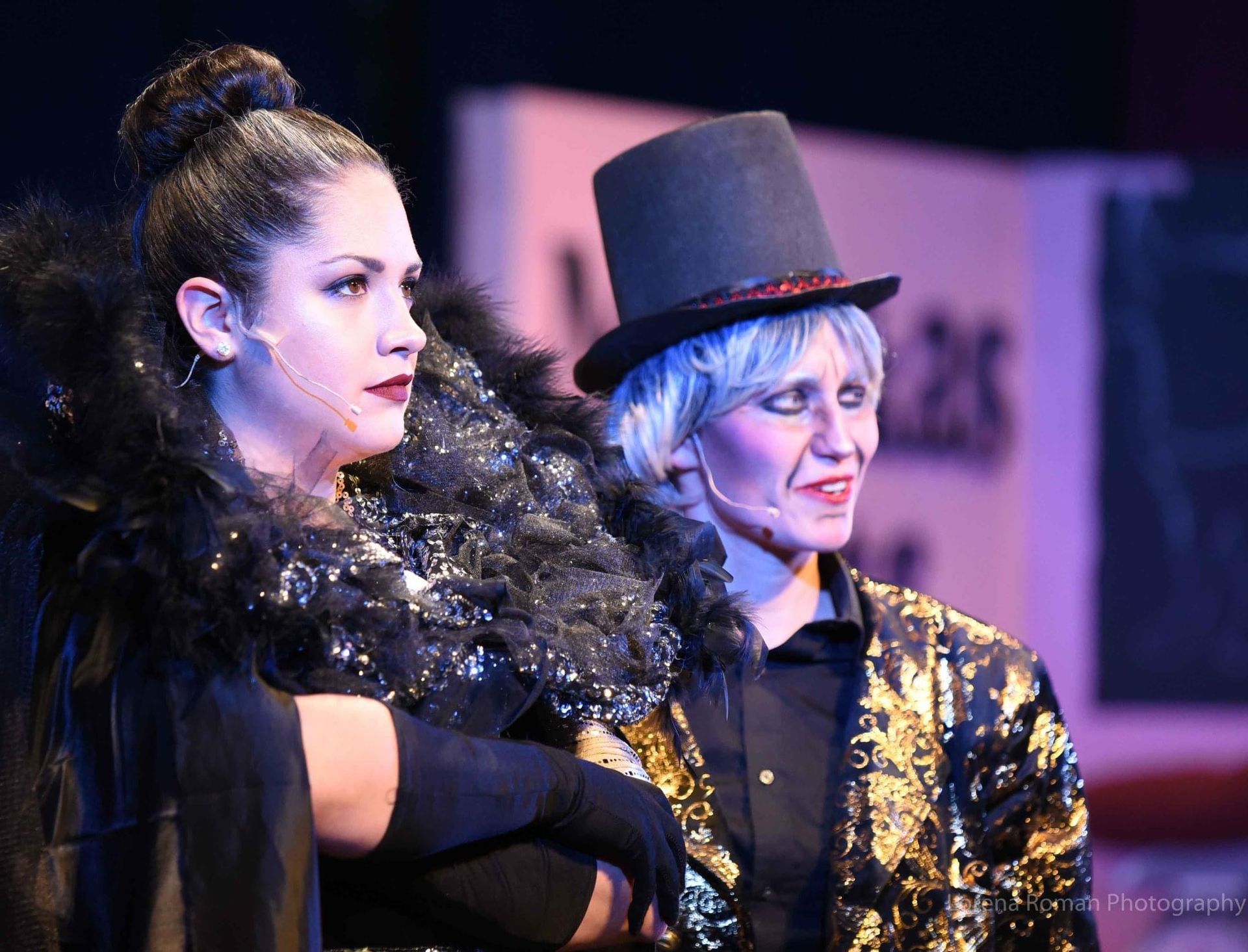 Two women are standing next to each other on a stage and one is wearing a top hat.