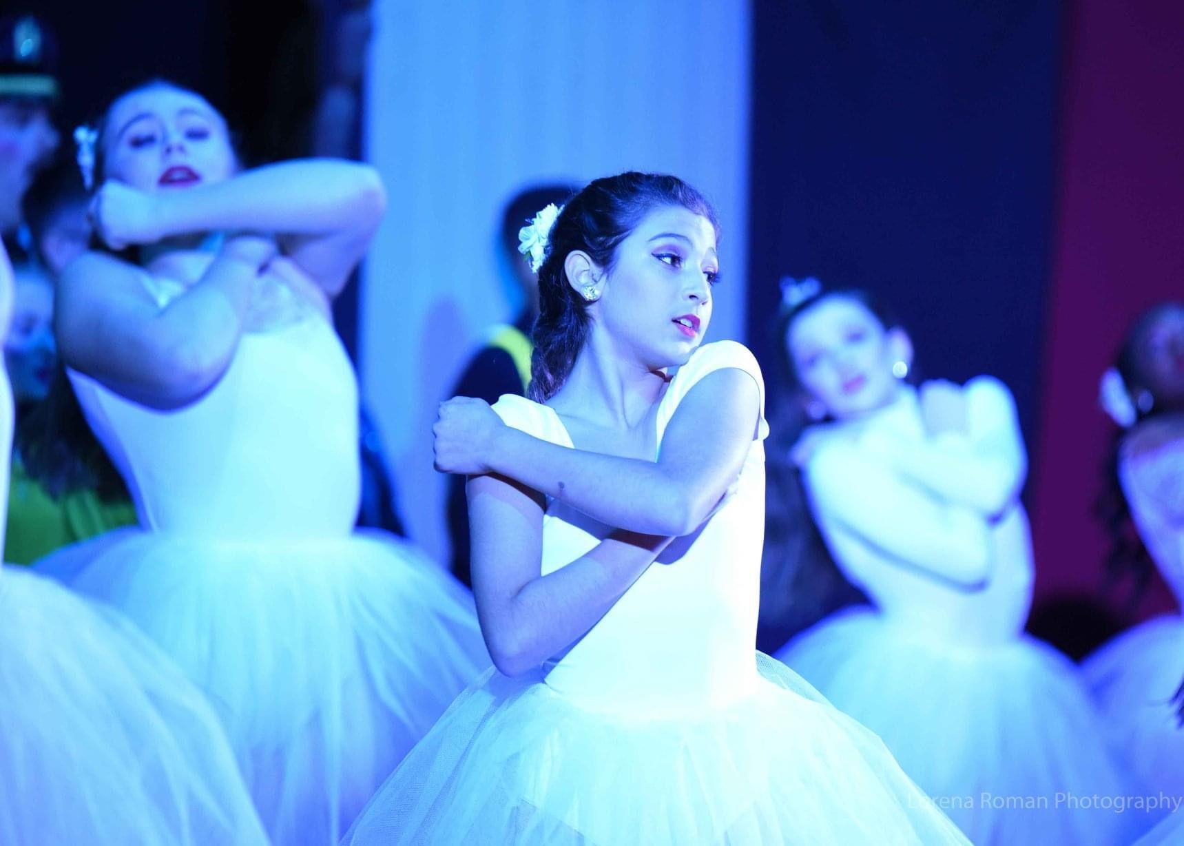 A group of young girls in white tutus are dancing on a stage