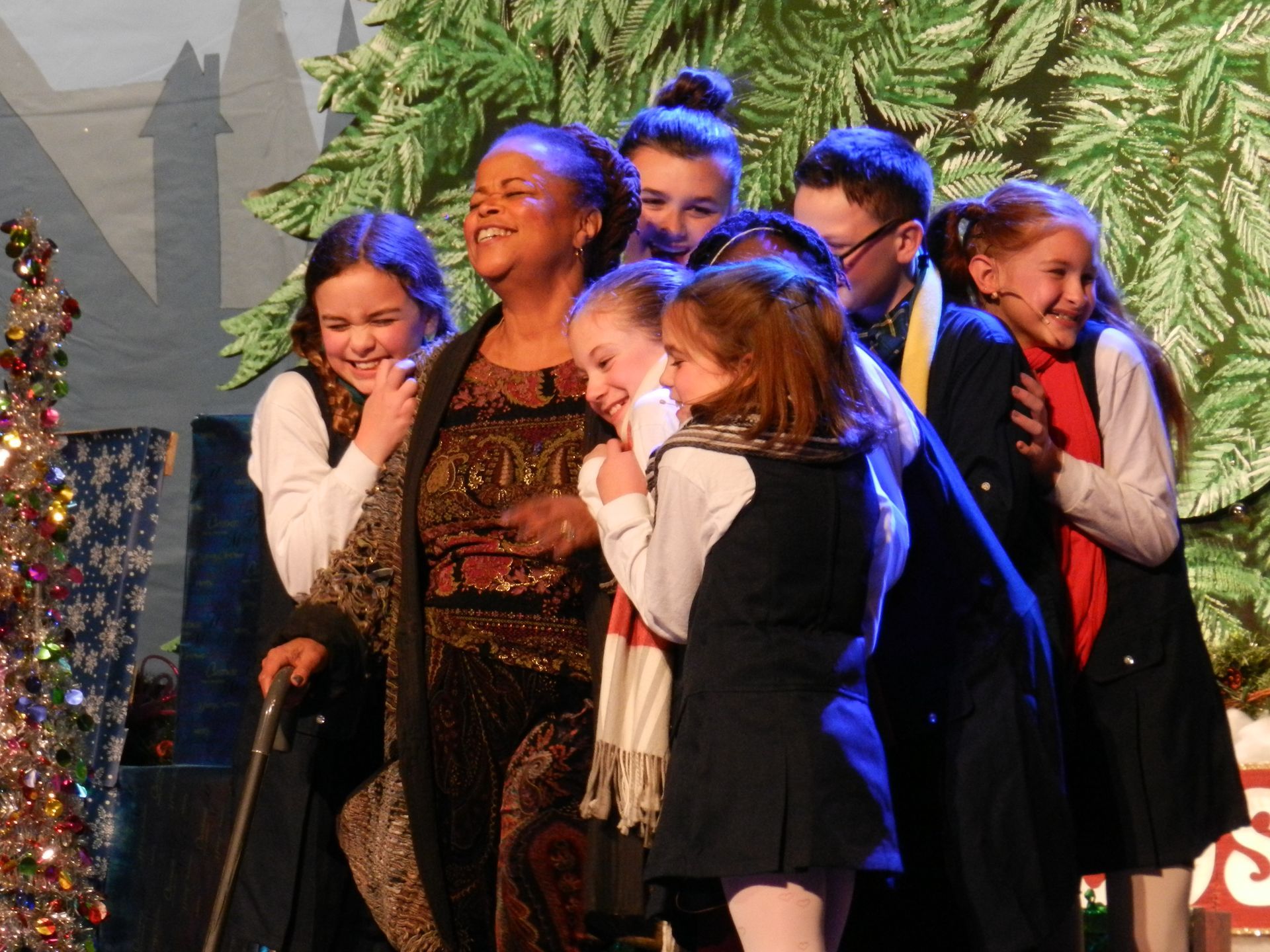 A woman with a cane is surrounded by children on a stage